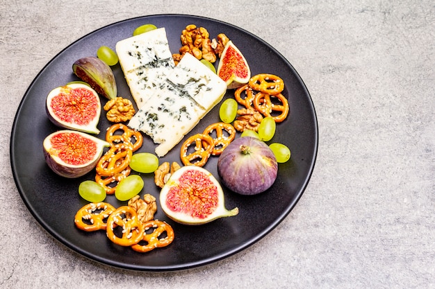 Plato de queso con queso azul, nueces, higos, uvas, pretzels