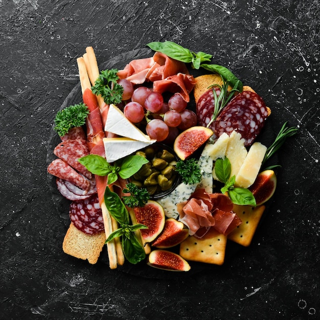 Un plato con queso salami prosciutto y bocadillos en un plato de piedra negra Antipasto Vista superior Comida italiana Espacio libre para su texto