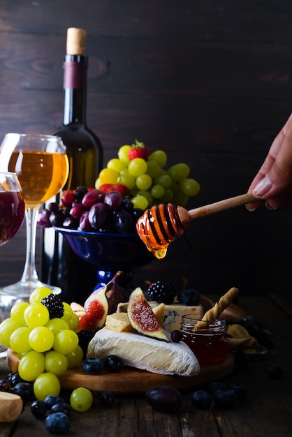 Plato de queso servido con vino, mermelada y en su mano un palo con miel.