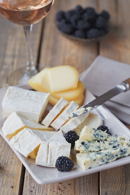 Plato de queso. Surtido de queso con frutos rojos y copa de vino rosado sobre fondo de madera.