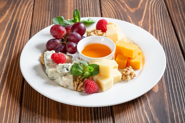 Foto plato de queso con uvas, miel y bayas