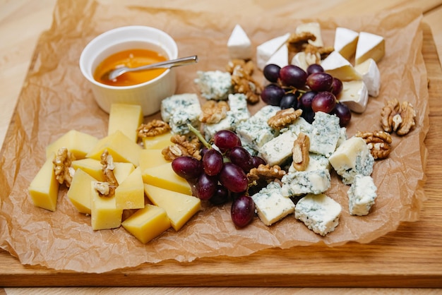 Plato de queso con uvas, miel y nueces en una tabla de madera