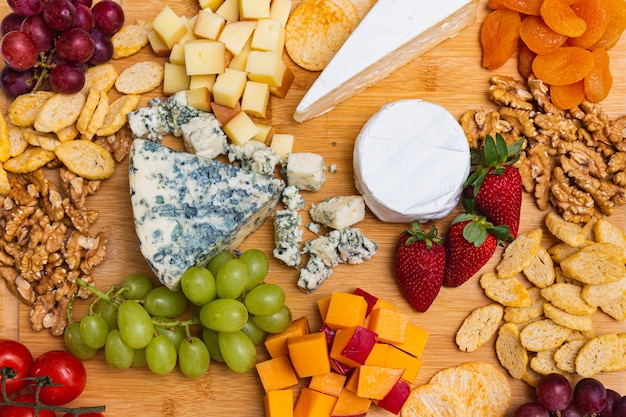 Plato de queso con variedad de aperitivos en la mesa. Platos de queso de fresa, albaricoque, uva y grano en la mesa