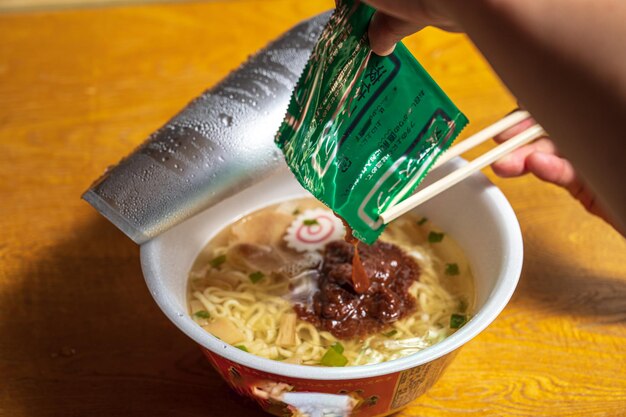 Un plato de ramen con una bolsa verde de palillos y una bolsa de fideos.