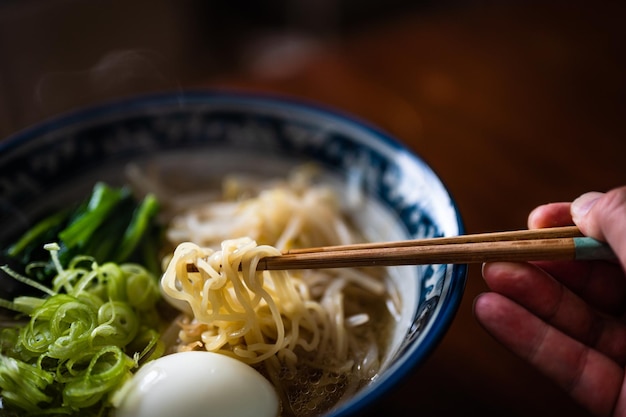 Un plato de ramen con palillos y un huevo.