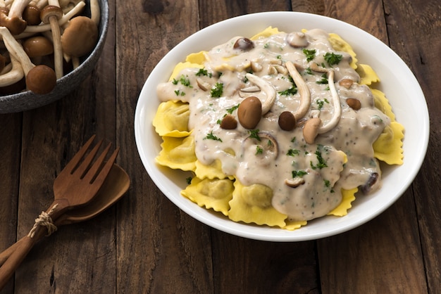 Plato de ravioles con salsa de crema y champiñones sobre mesa de madera