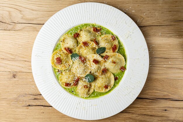 Un plato de ravioli con salsa verde y hojas de albahaca sobre una mesa de madera.