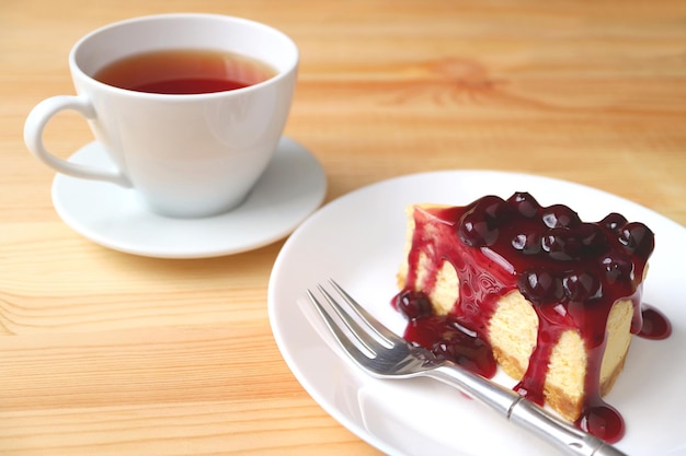 Plato de una rebanada de tarta de queso con salsa de arándanos y una taza de té caliente servido en una mesa de madera