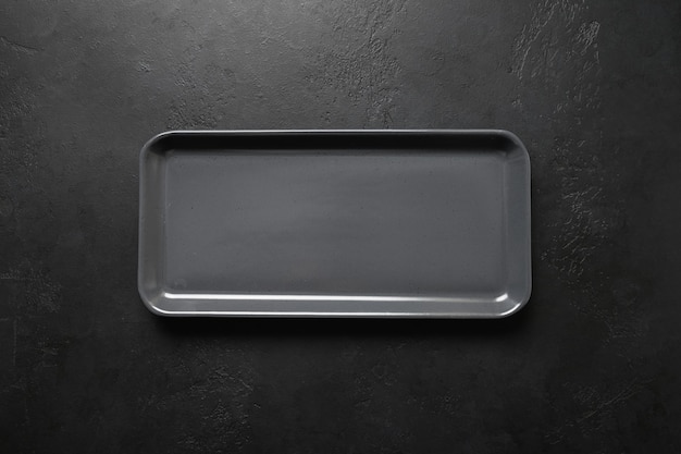 Plato rectangular moderno negro vacío sobre fondo negro, material de cocina, plano para cocinar como fondo.