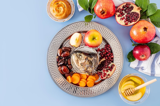 Un plato con un regalo de Año Nuevo para las vacaciones de Año Nuevo Rosh Hashanah granada miel fechas rodajas de manzana y zanahorias Fondo azul