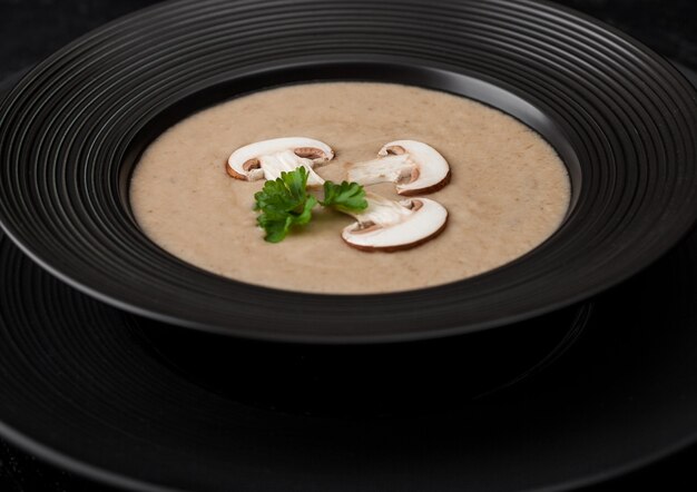 Plato de restaurante negro de cremosa sopa de champiñones y castañas sobre fondo negro.