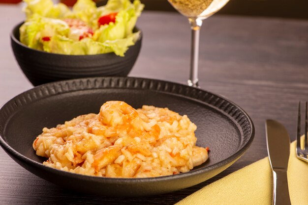 Plato de risotto de camarones, ensalada de lechuga y tomates cherry y una copa de vino blanco