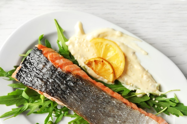 Plato con rodaja de delicioso salmón a la parrilla y salsa de pescado en la mesa