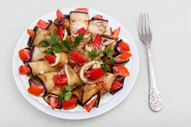 Plato de rodajas de berenjena frita con tomate y salsa de queso decorado con hojas de perejil en la placa blanca.