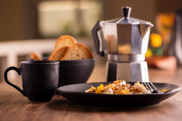 Plato con rodajas de plátano con granola, fruta confitada y miel, tostadas y una taza de café.