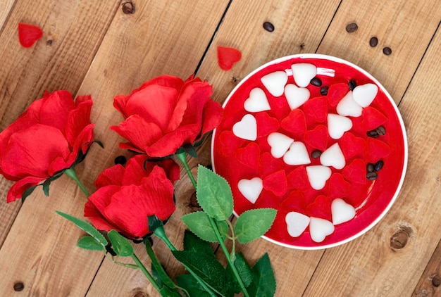 Plato rojo con dulces en forma de corazón y rosas rojas sobre un fondo de maderaVista superior