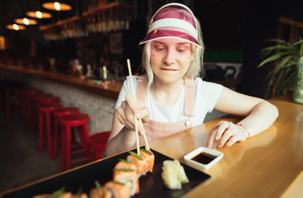 Plato de rollos de sushi en restaurante con mujer sosteniendo palillos