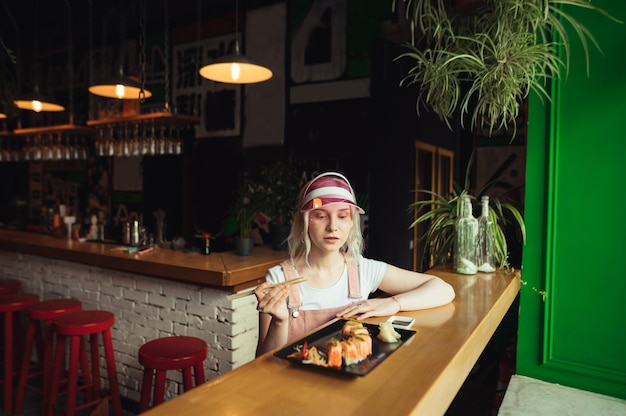 Plato de rollos de sushi en restaurante con mujer sosteniendo palillos