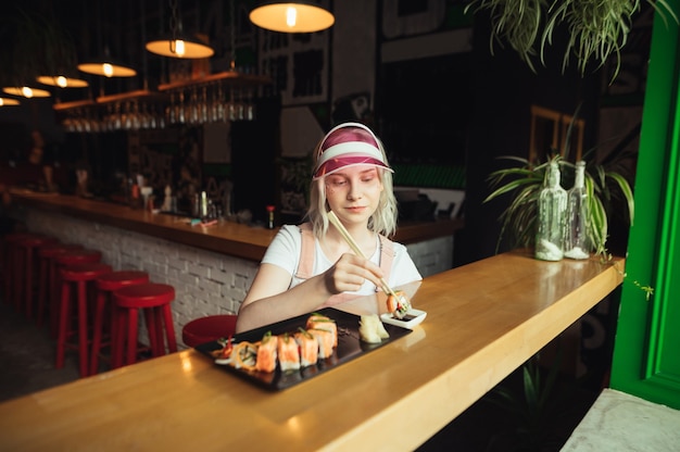 Plato de rollos de sushi en restaurante con mujer sosteniendo palillos