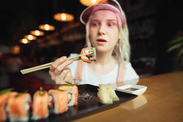 Plato de rollos de sushi en restaurante con mujer sosteniendo palillos