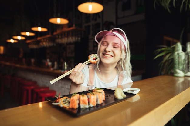 Plato de rollos de sushi en restaurante con mujer sosteniendo palillos