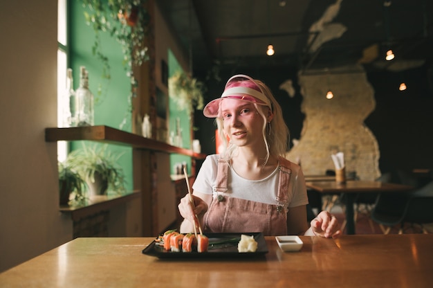 Plato de rollos de sushi en restaurante con mujer sosteniendo palillos