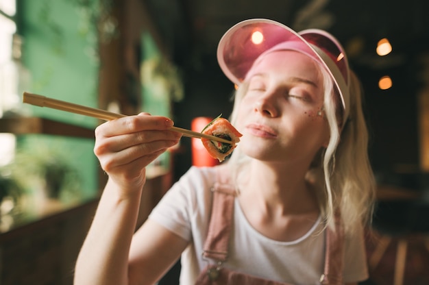 Plato de rollos de sushi en restaurante con mujer sosteniendo palillos