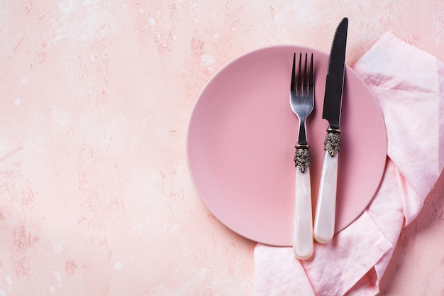 Plato rosa, cubiertos y servilleta en la vista superior de la mesa de piedra