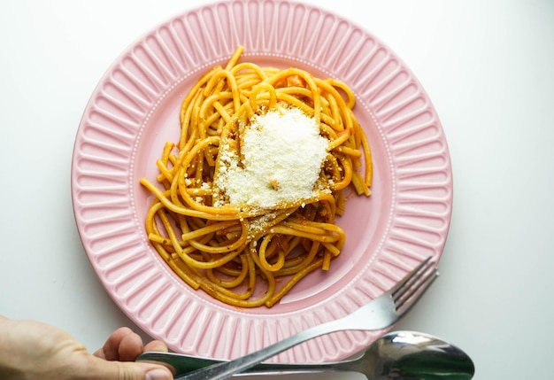 Un plato rosa de espaguetis frescos con salsa de tomate y queso parmesano