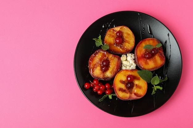 Plato con sabroso melocotón a la plancha sobre fondo rosa