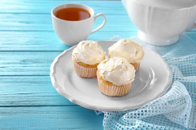 Plato con sabrosos cupcakes de vainilla y taza de té en la mesa