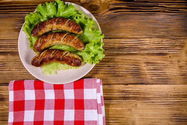 Plato con salchichas asadas y hojas de lechuga en una mesa de madera Vista superior