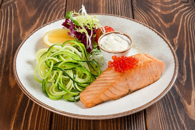 Foto plato de salmón al vapor con caviar rojo y verduras en la mesa de madera