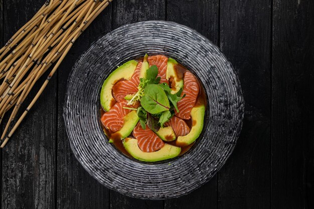 Un plato con salmón picado y aguacate sobre una mesa oscura