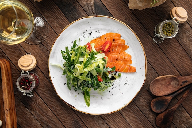 Plato de salmón en rodajas salado y ensalada verde sobre fondo de madera