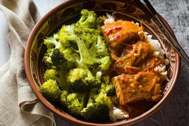 Plato de salmón tailandés en salsa de coco con brócoli fresco y arroz en un recipiente de arcilla con palillos alimentos saludables con vitamina B5