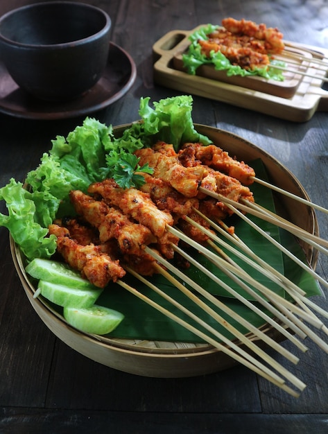 Un plato de satay de pollo en un palo de bambú con una guarnición de verduras de hoja.