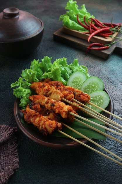 Un plato de satay de pollo con un plato de verduras.