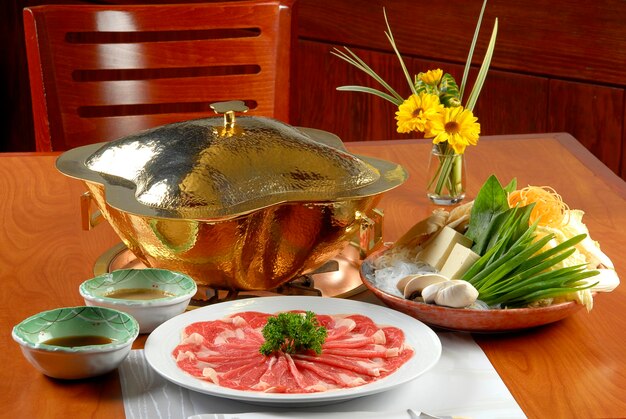 Plato de shabushabu con salsas de fideos de verduras tofu y quemador de fondue en comida de mesa de madera