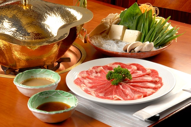 Plato de shabushabu con salsas de fideos de verduras tofu y quemador de fondue en comida de mesa de madera