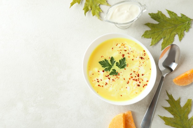 Plato de sopa de calabaza e ingredientes en la mesa con textura blanca