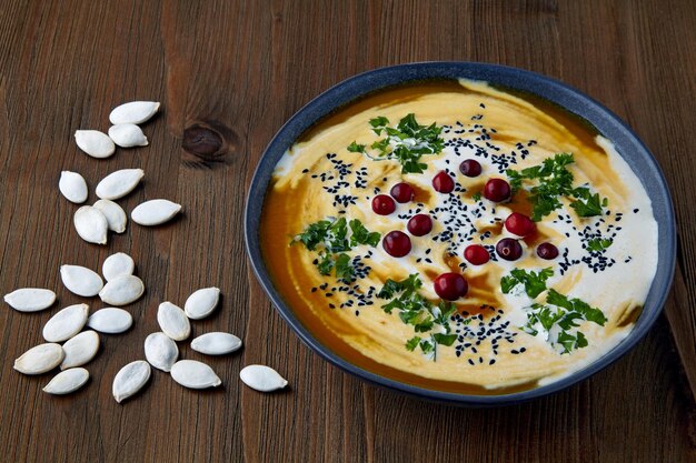 Un plato de sopa cremosa de calabaza con semillas de comino negro crema, hierbas y arándanos sobre una mesa de madera