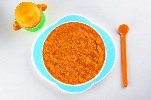 Plato de sopa cremosa de zanahoria baby y botella aislado en blanco