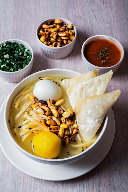 Foto plato de sopa de pollo con fideos fritos de huevos amarillos patata cancha serrana acompañado de cebolla china y rocoto