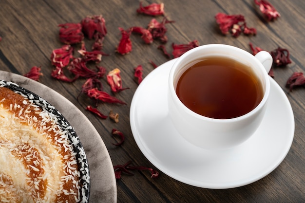 Plato de tarta dulce con chispas de coco, pétalos de rosa y taza de té en la superficie de madera