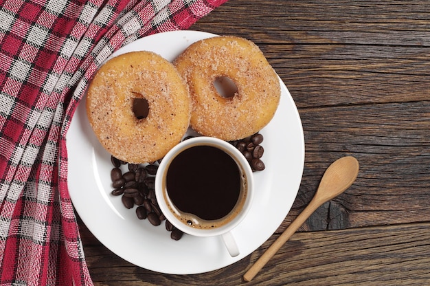 Plato con taza de café y donuts para desayunar en una mesa rústica de madera, vista superior