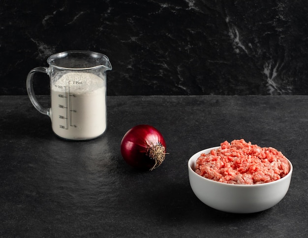 Plato con taza medidora de cebolla roja de carne molida fresca con harina en un espacio de fondo negro gris para textxA