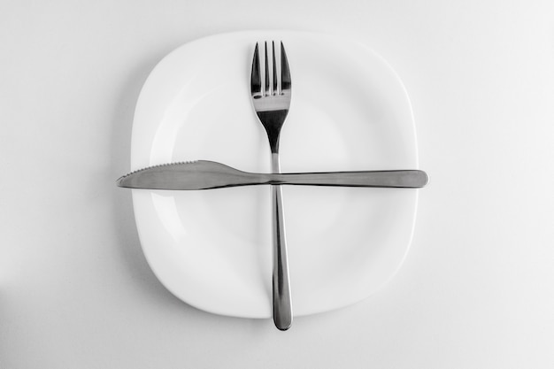 El plato, el tenedor y el cuchillo vacíos se encuentran cruzados sobre un blanco.