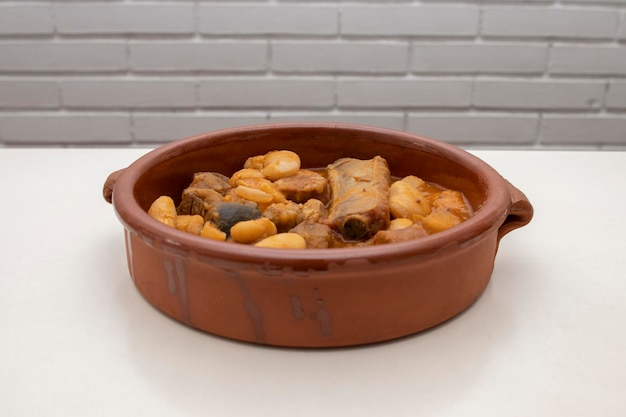 Foto un plato de terracota con fabada asturiana, un guiso de judías típico español sobre un fondo blanco.