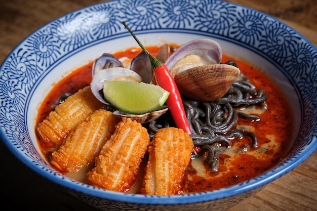 Plato típico de ramen caliente con caldo de pescado en un cuenco con fideos negros calamares chilli almejas